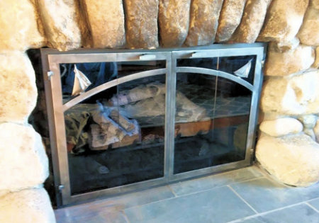 Harborside Horizon fireplace doors black frame with Sailboat motif. vice bi fold natural iron doors and smoked glass. Comes with slide mesh installed on stone